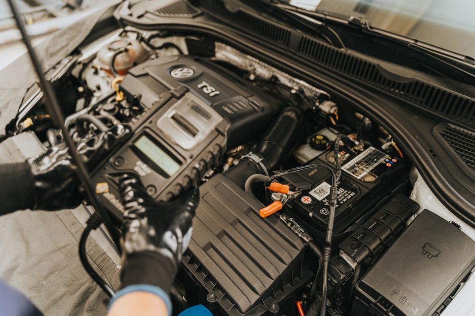Mains gantées tenant un appareil de diagnostic branché sur le moteur d'une voiture