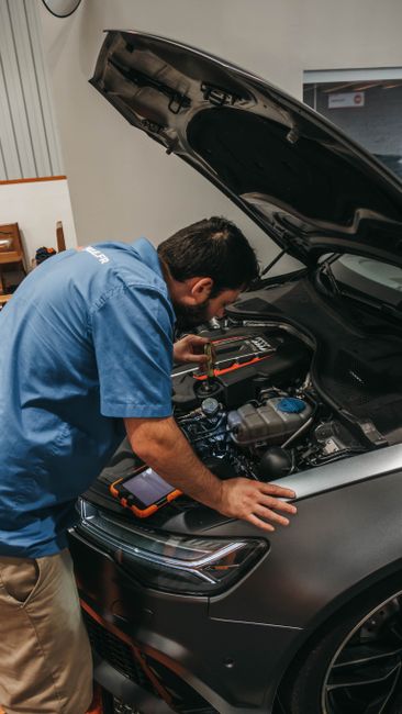 Mécanicien penché sur le moteur d'une voiture capot ouvert, tablette de diagnostic posée sur l'aile